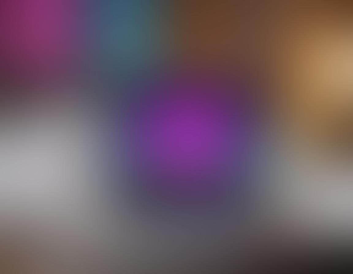 A sleek modern laptop with a vibrant glowing screen displaying various adult film thumbnails, surrounded by a luxurious bedroom setting with plush pillows and ambient lighting. Include a stylish glass of wine and a remote control casually placed nearby, giving an inviting atmosphere that suggests relaxation and entertainment. The overall mood should be enticing yet polished. super-realistic. vibrant colors. soft focus.